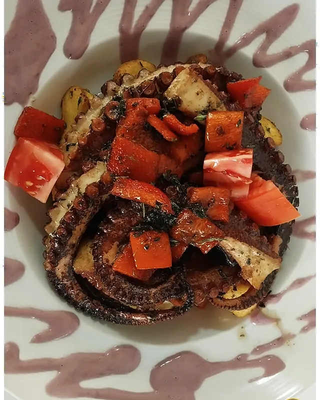 Pulpo con tomate picado sobre un plato decorado con salsa de aceituna