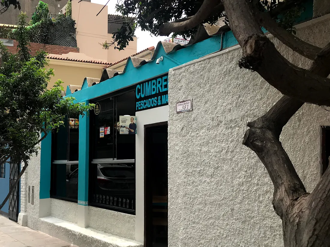 La fachada de Cumbremar desde la vereda: pared blanca, alero turquesa y su letrero, en la Calle Bolívar 381